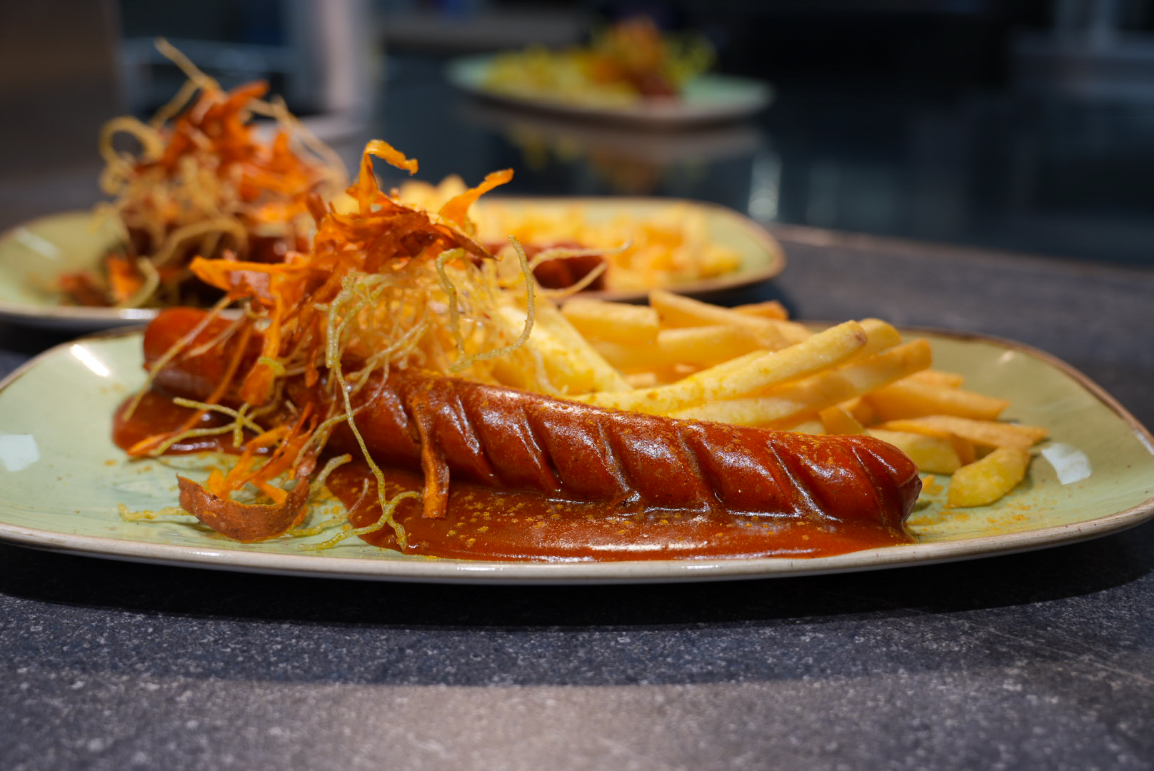 Currywurst mit knusprigen Kartoffelspalten und karamellisierten Zwiebelstreifen auf einem Teller.
