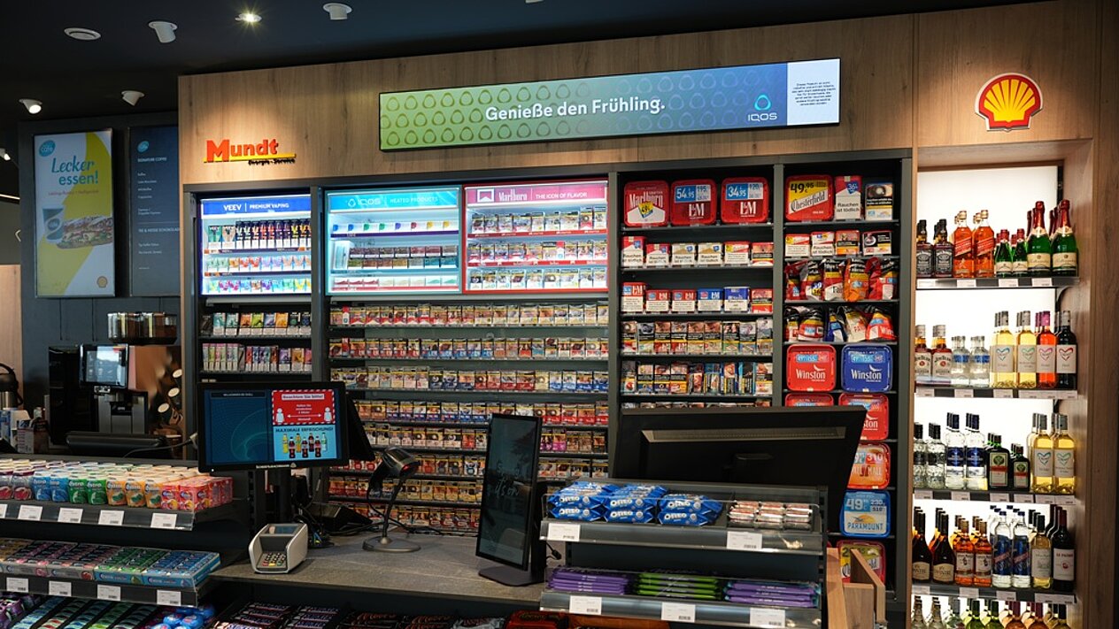 Moderner Verkaufsstand mit Tabakprodukten, Snacks und Getränken, darunter Promotions für Frühlingsangebote.