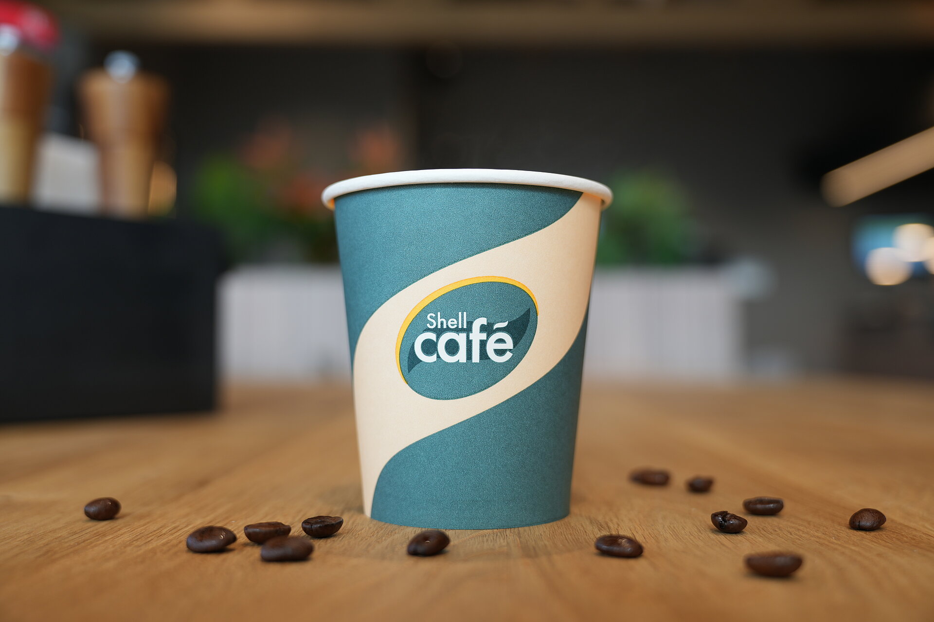 Ein Kaffeebecher von Shell Café mit kraftigem Kaffee auf einem Holztisch