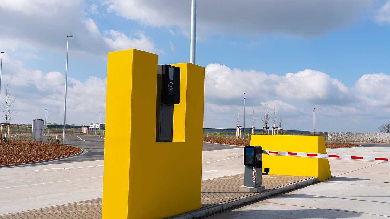 Automatische Schranke mit Zahlterminal in gelber Farbe an einer Parkplatzausfahrt unter blauem Himmel.