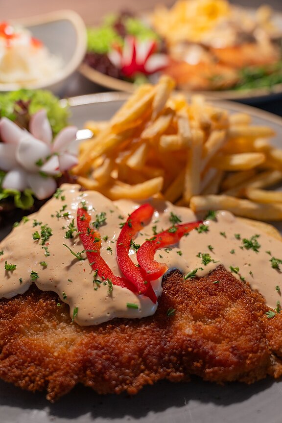 Ein Schnitzel mit Pommes und einer cremigen Soße, auf einem Teller angerichtet.