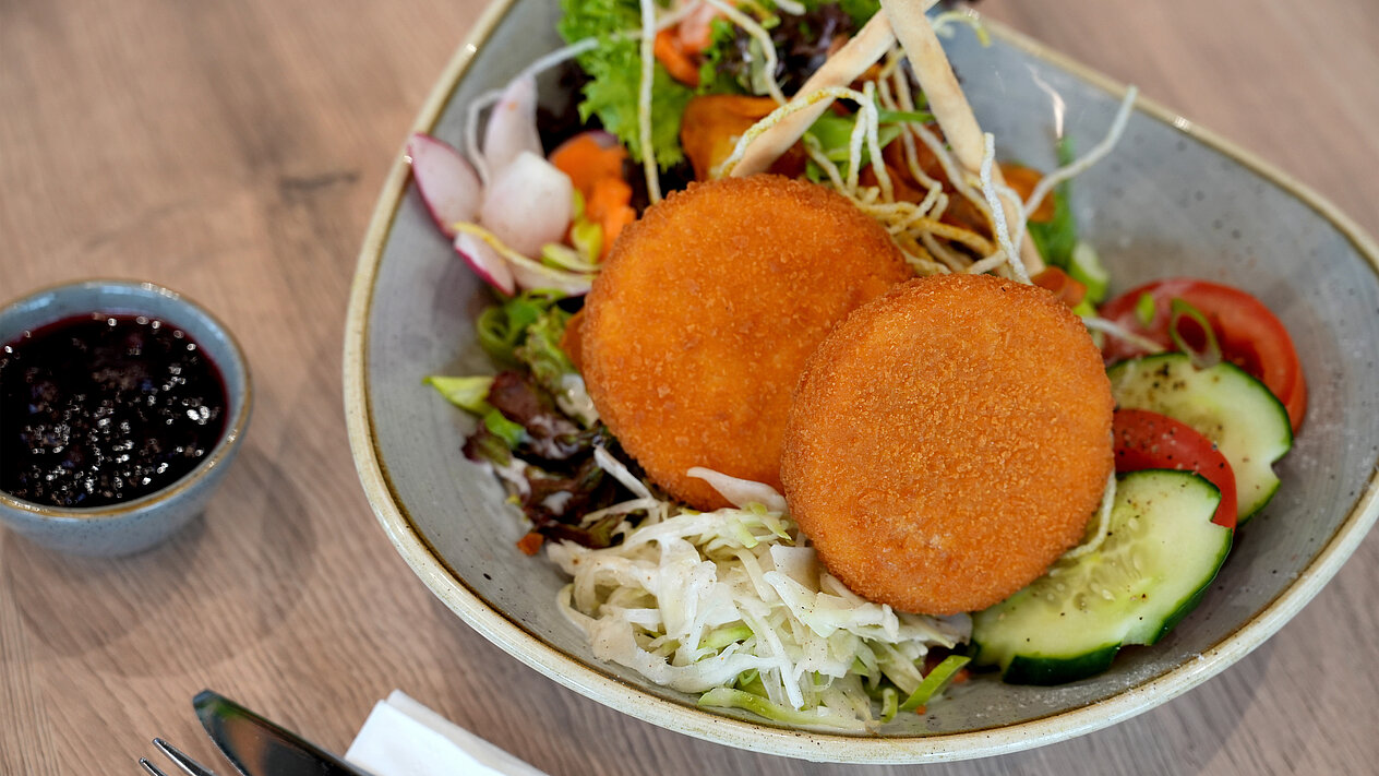 Gold gebackene Camemberts auf frischem Salat mit Gurke, Tomate und Radieschen, serviert mit Preiselbeerdip.