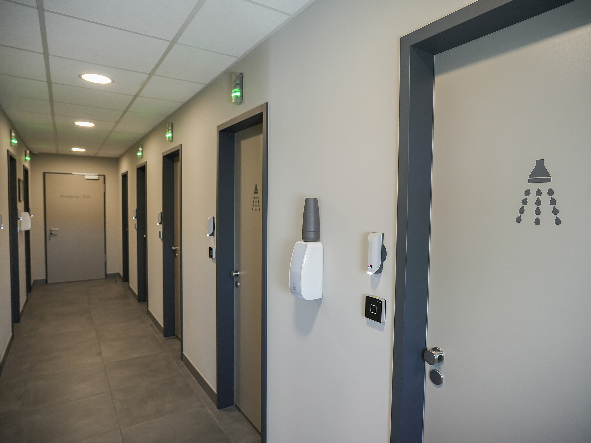 Ein gang mit vielen Türen auf der linken und rechten Seite, die zu den Duschräumen führen. Über den Türen ist eine Lichtanzeige, die anzeigt, ob die Dusche besetzt oder frei ist.
