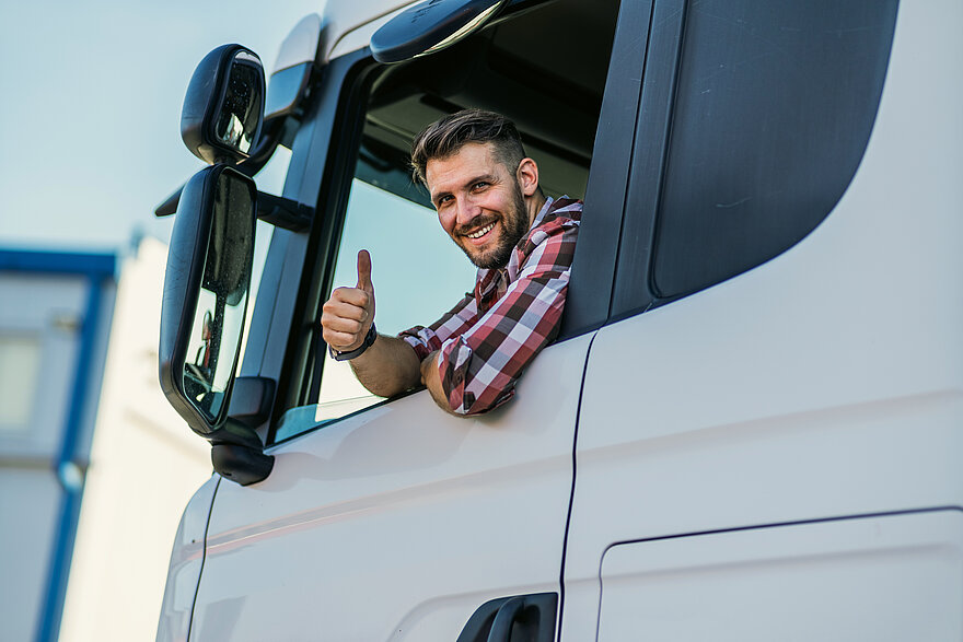 LKW-Fahrer zeigt mit Daumen hoch Ein zufriedener LKW-Fahrer gibt aus dem Führerhausfenster ein Daumen-hoch-Signal bei Sonnenschein.