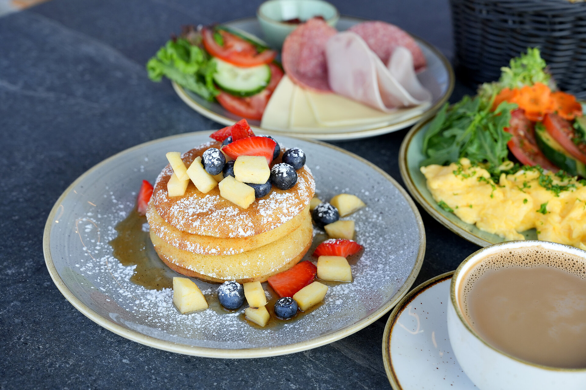 Detailansicht eines Frühstückstisches mit Pancakes, Rührei, Kaffee und Aufschnitt