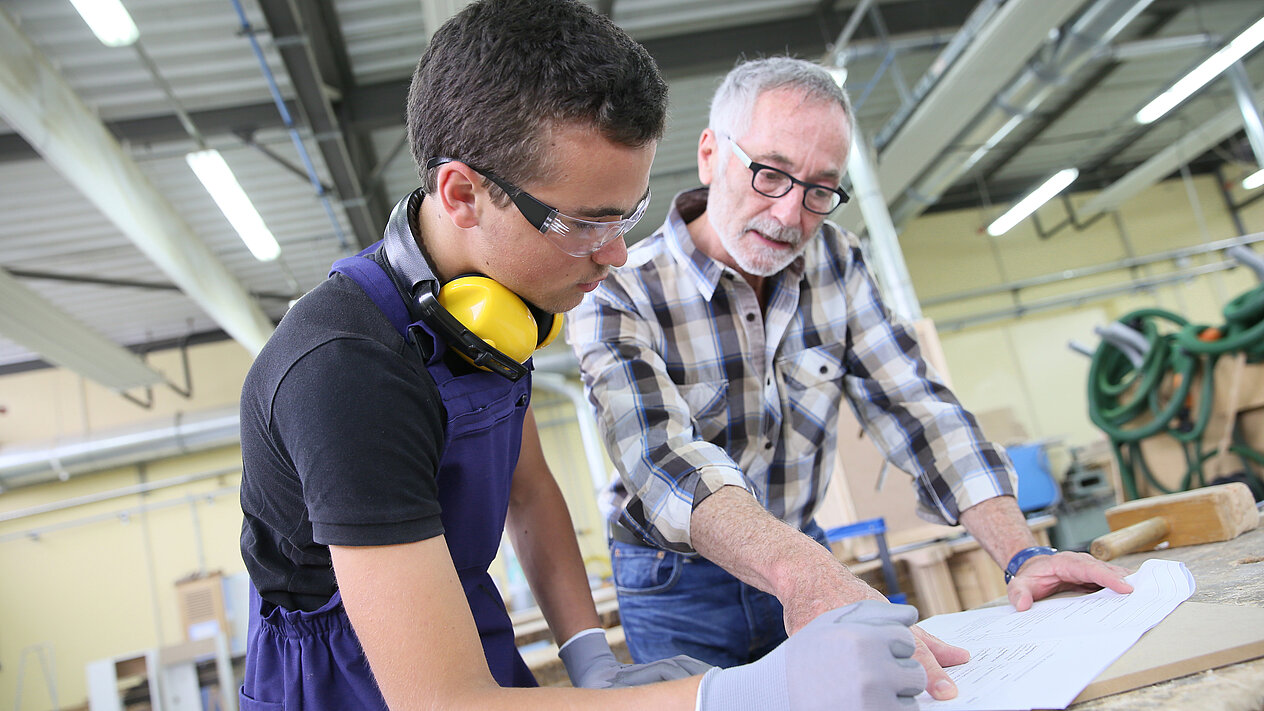 Ein Handwerker und sein Vorarbeiter stehen an einem Tisch und besprechen einen Bauplan.