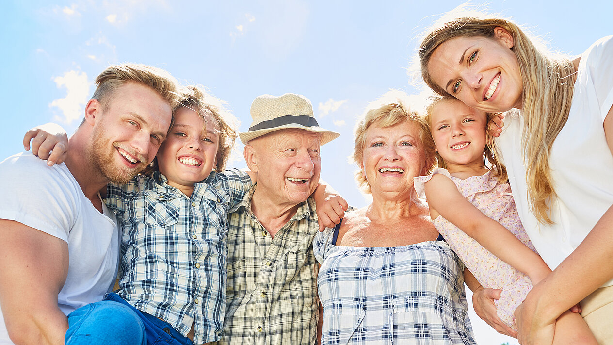 Eine drei Generationen Familien, bestehend aus Vater, Sohn, Großvater, Großmutter, Tochter und Mutter umarmen und freuen sich.