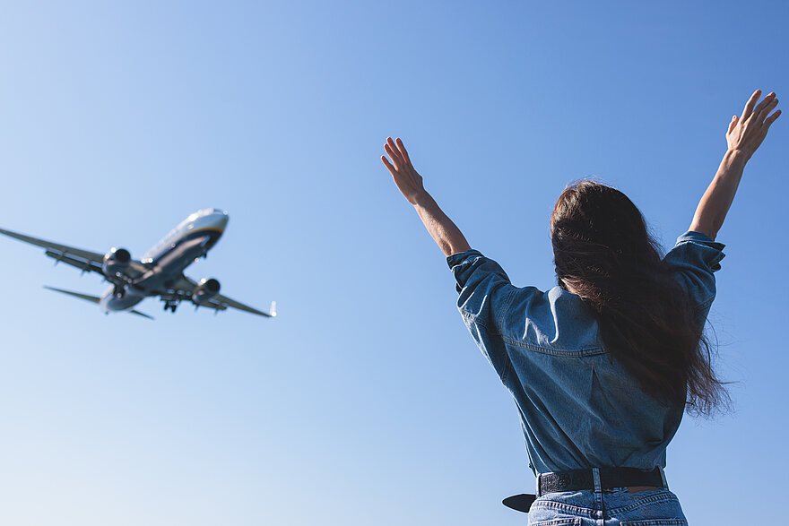 Man sieht eine Planespotterin von hinten, die einem fliegenden Flugzeug zujubelt.