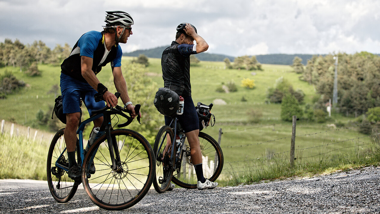 Zwei Radfahrer stehen mit ihren Fahrrädern in der Natur und machen kurz Halt