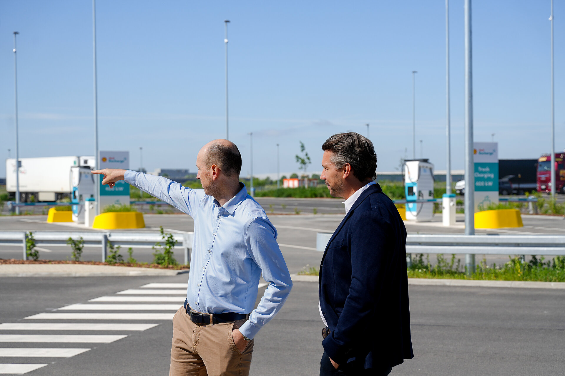 Zwei Geschäftsleute begutachten eine moderne Schnellladestation für Elektro-Lkw auf einem Rastplatz.