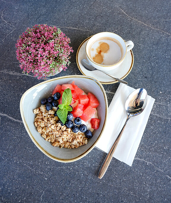 Tisch mit Müslibowl, frischem Obst und Cappuccino