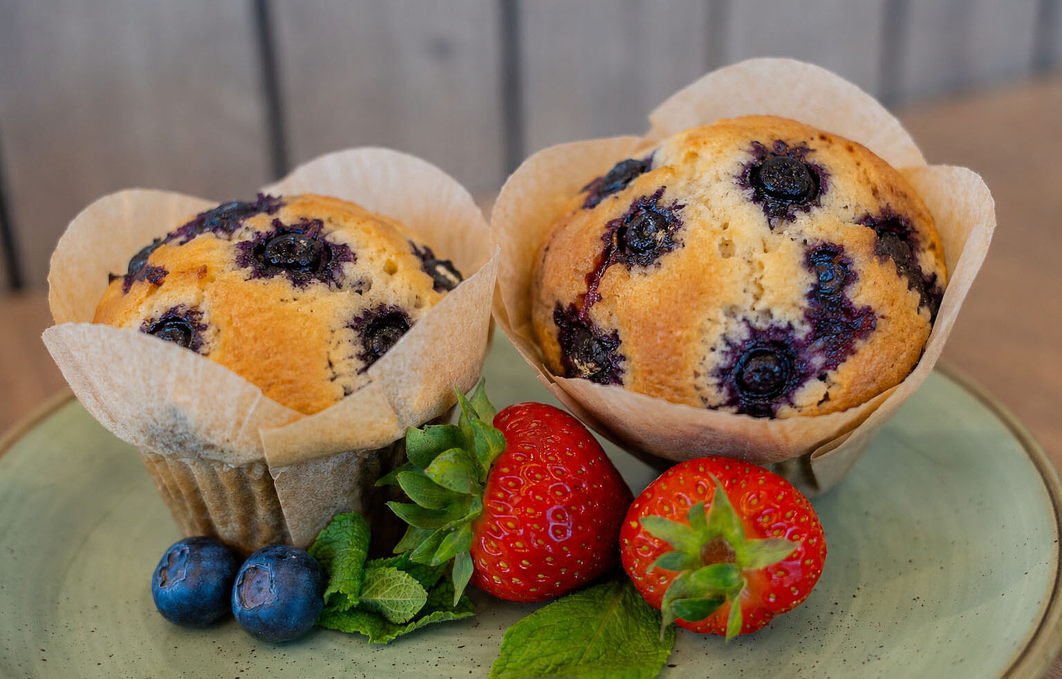 Zwei fluffige Blaubeermuffins auf einem Teller, dekoriert mit Erdbeeren und Heidelbeeren