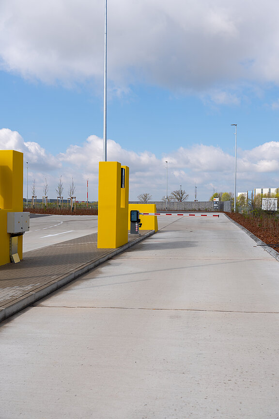 Eine gelbe Schranke steht an einem Parkplatz, umgeben von einer klaren blauen Himmel und sanften Wolken.