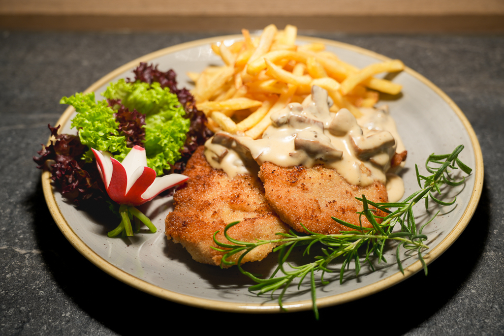 Ein appetitliches Gericht: Schnitzel in Sauce, begleitet von goldenen Pommes und einem frischen, dekorativen Salat.